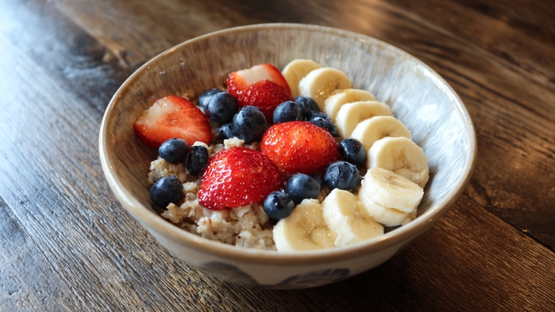 Činija zobenih pahuljica sa svežim jagodama, borovnicama i kriškama banane na drvenom stolu