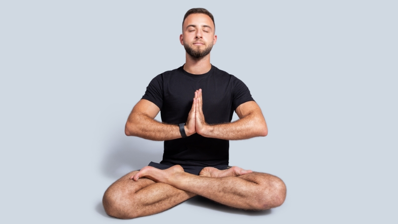 Mladić sedi u lotos položaju sa zatvorenim očima i spojenim dlanovima